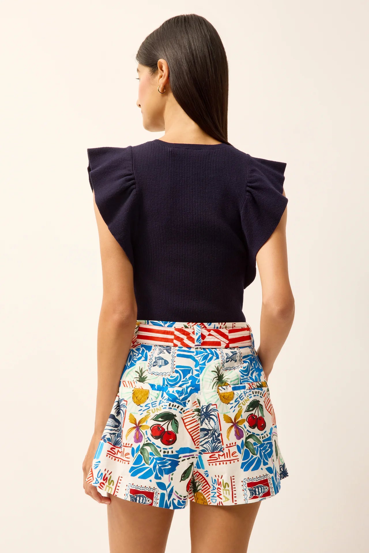 Woman wearing a navy top and colorful patterned shorts on a plain background