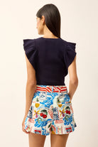 Woman wearing a navy top and colorful patterned shorts on a plain background