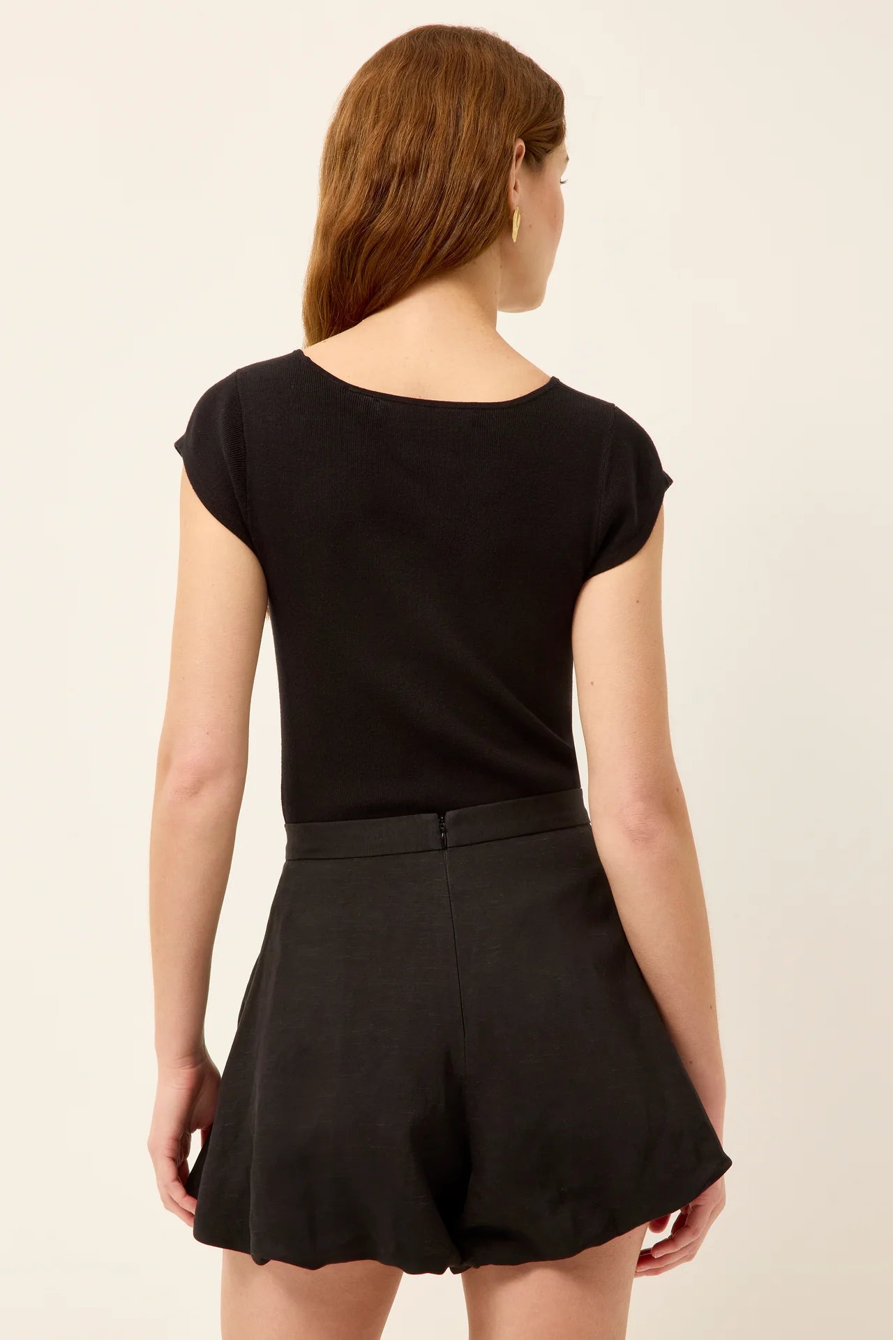 Woman wearing a black top and black shorts on a beige background