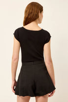 Woman wearing a black top and black shorts on a beige background