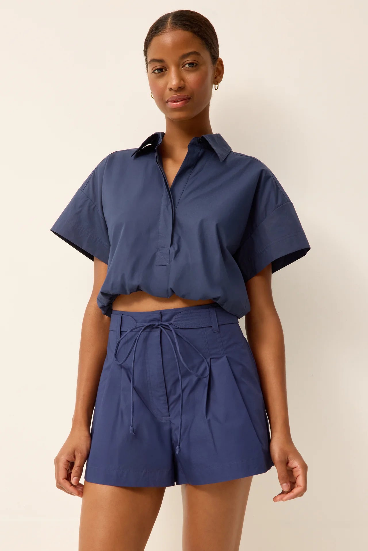 Woman wearing a blue outfit with a matching shirt and shorts on a beige background