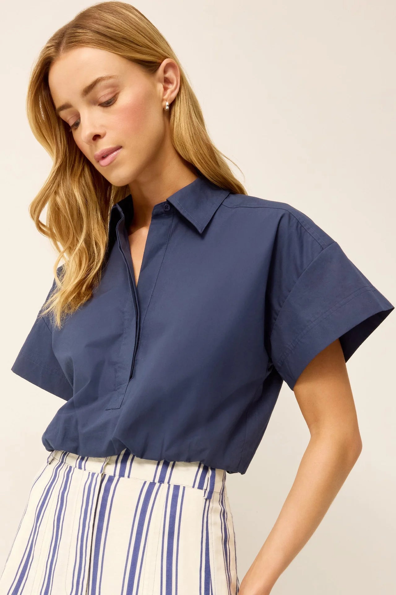 Woman wearing a blue short-sleeve shirt and striped pants on a plain background