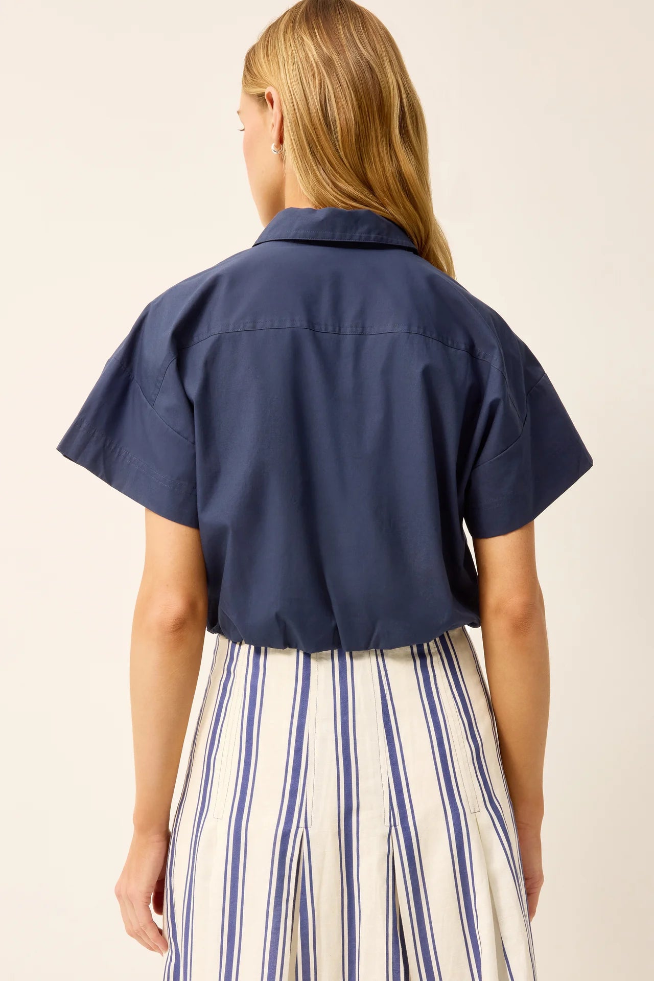 Person wearing a navy blue short-sleeve shirt with a beige background