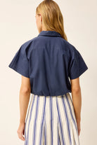Person wearing a navy blue short-sleeve shirt with a beige background