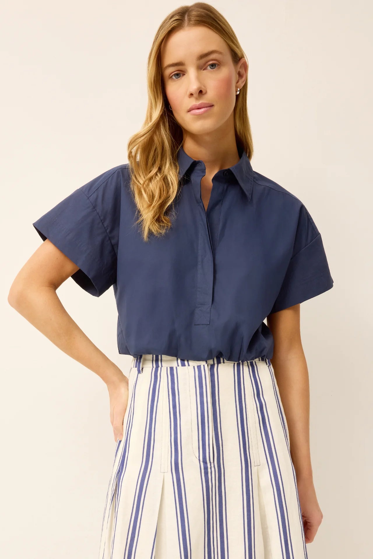 Woman wearing a navy blue short-sleeve blouse and striped pants on a beige background
