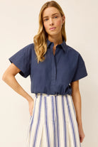 Woman wearing a navy blue short-sleeve blouse and striped pants on a beige background