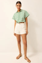 Woman wearing a green and white striped shirt and white shorts on a plain background