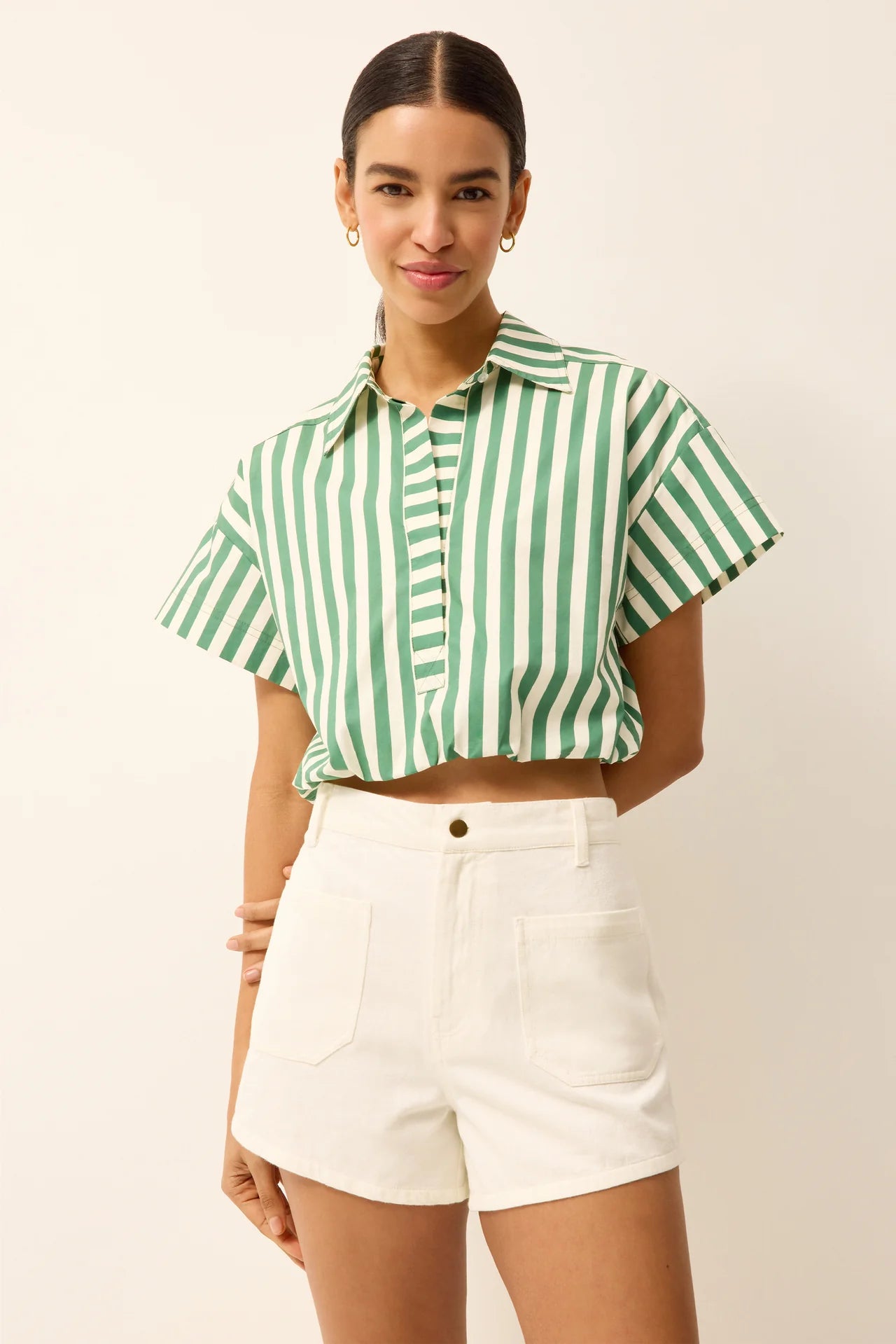 Woman wearing a green and white striped shirt and white shorts on a beige background