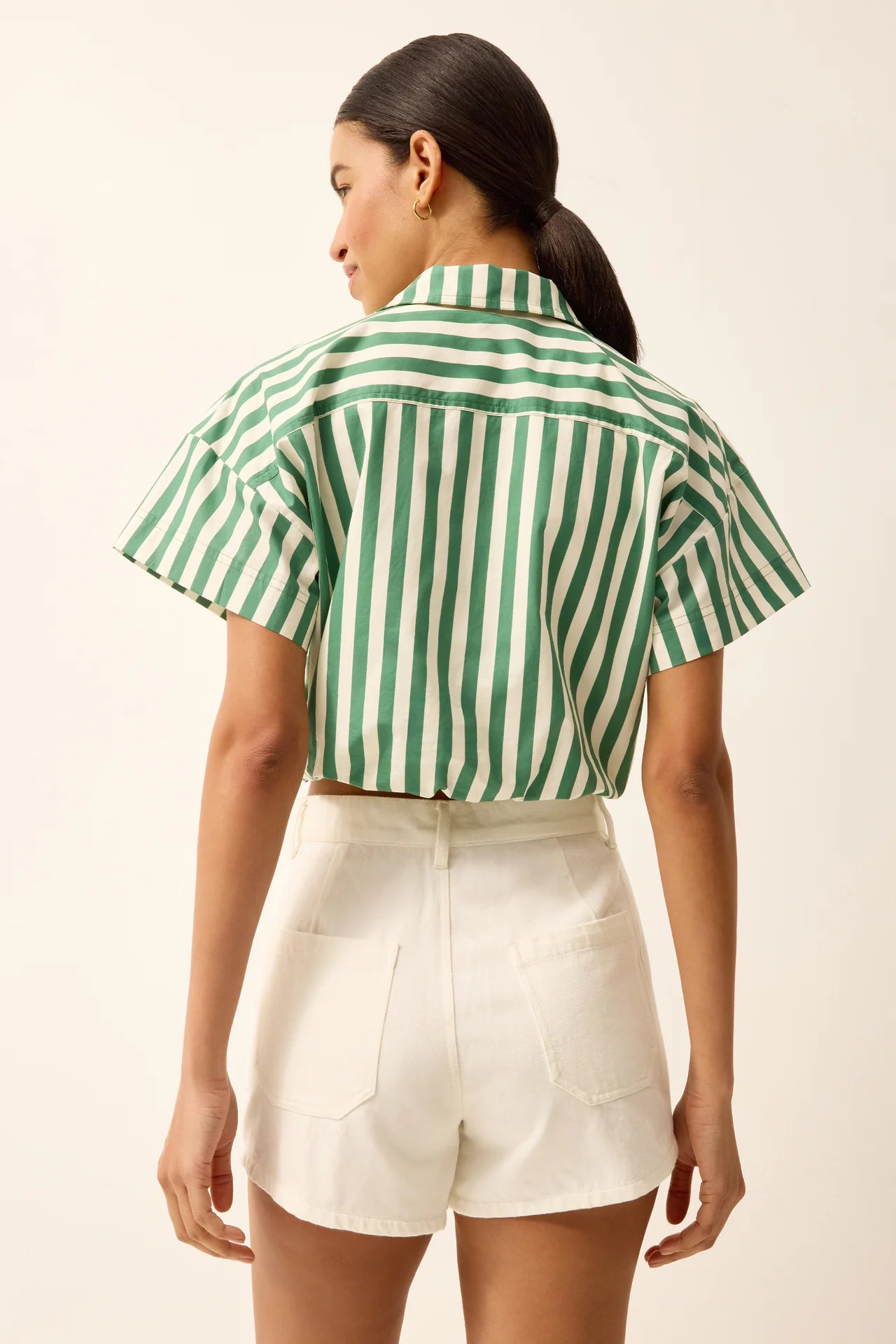 Woman wearing a green and white striped shirt and white shorts on a beige background