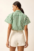 Woman wearing a green and white striped shirt and white shorts on a beige background