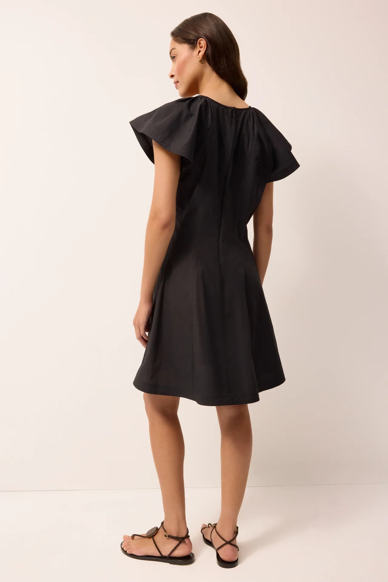 Woman wearing a black dress with ruffled shoulders on a white background