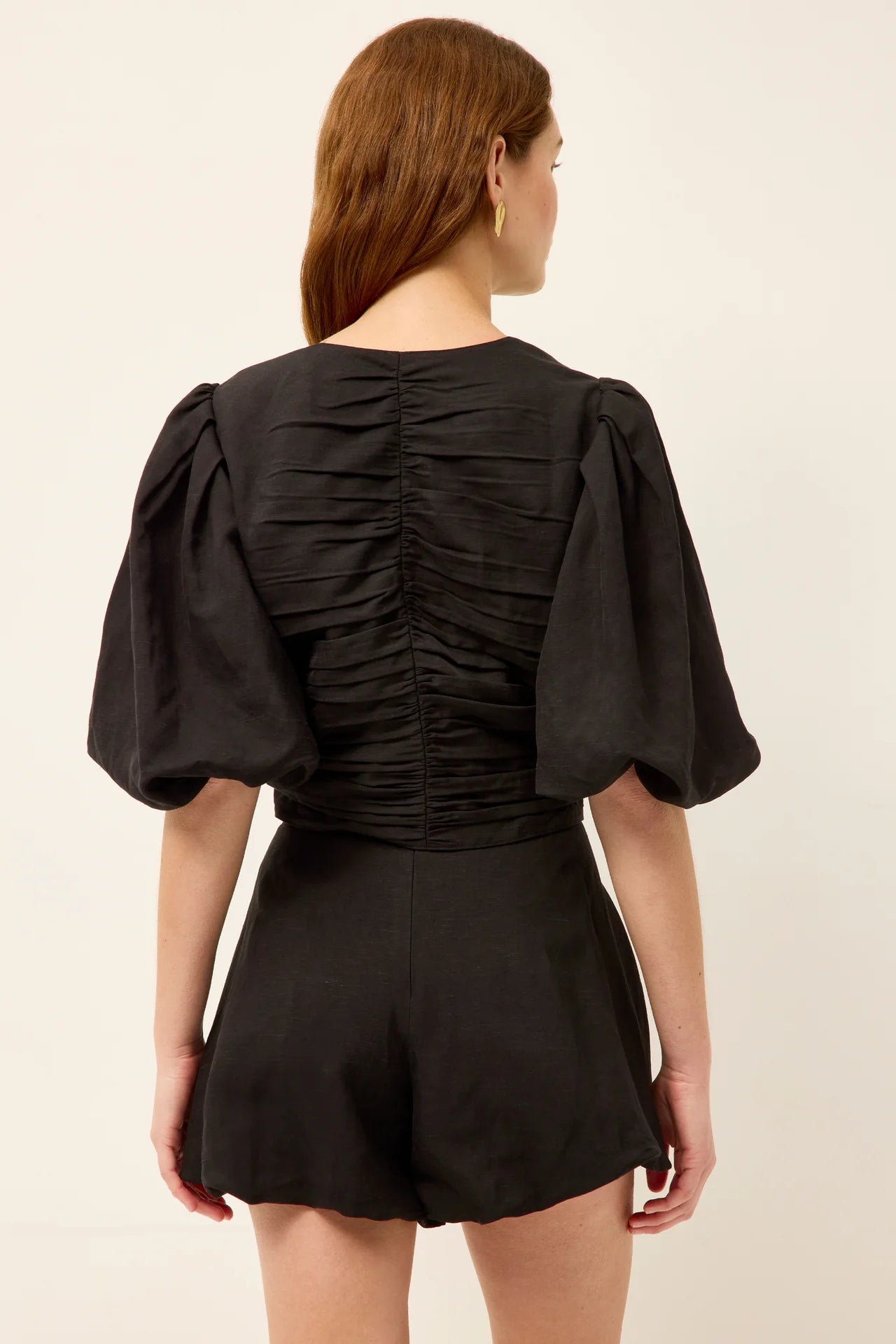 Woman wearing a black outfit with puffed sleeves on a beige background