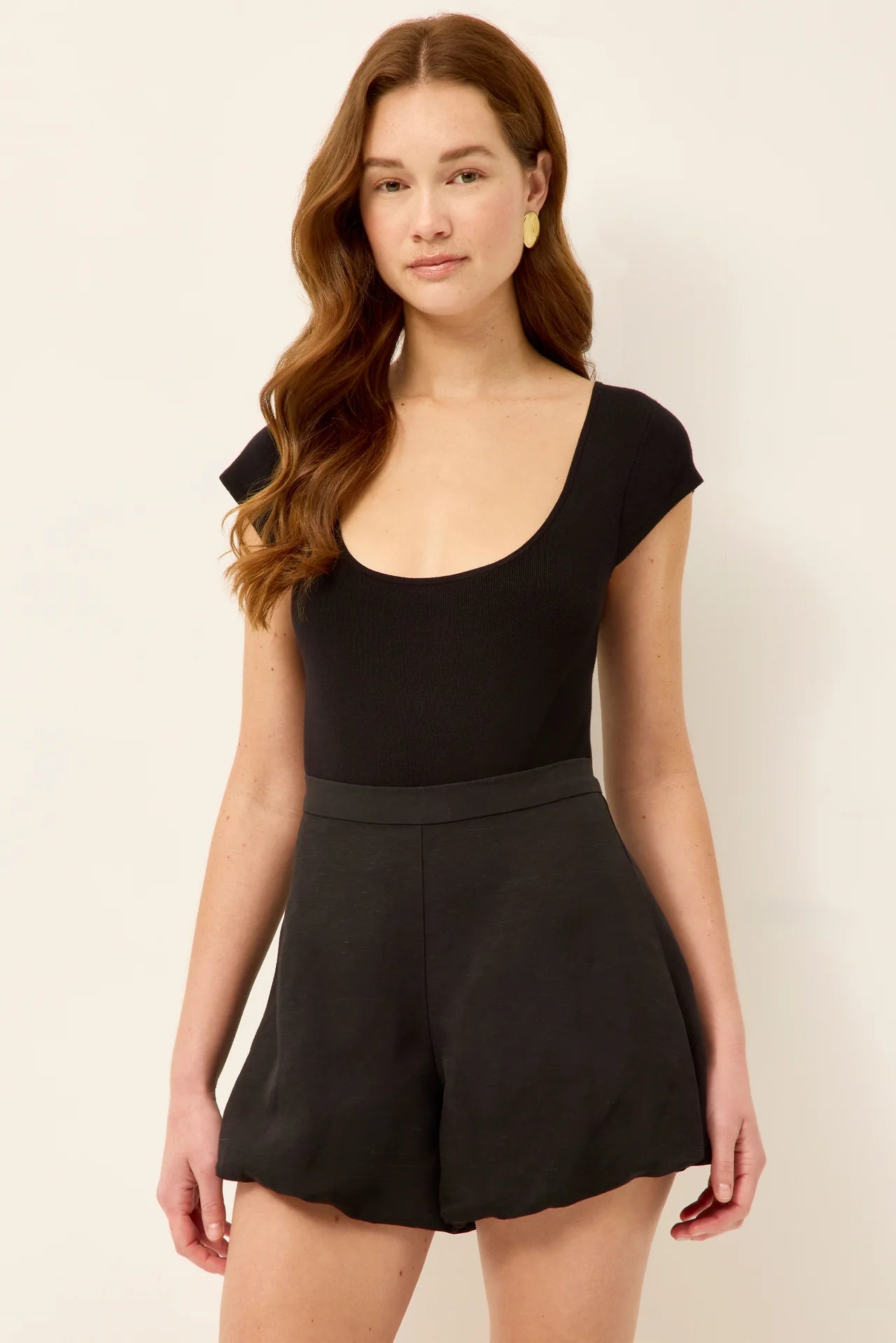 Woman wearing a black romper against a beige background