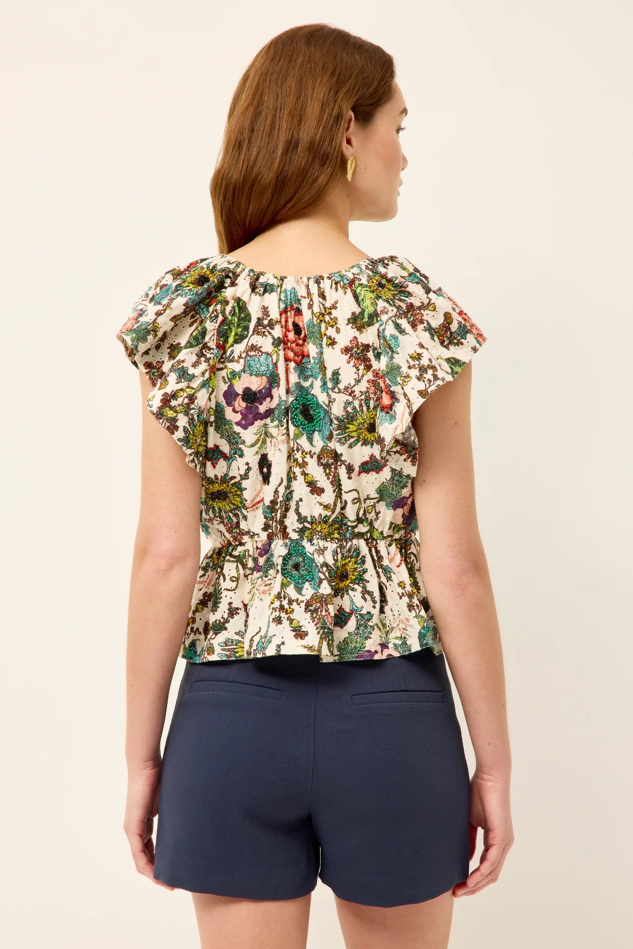 Woman wearing a floral top and navy shorts on a beige background