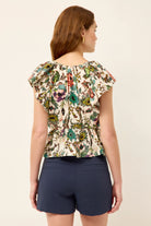 Woman wearing a floral top and navy shorts on a beige background