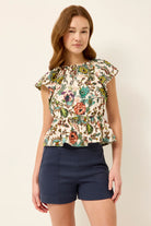 Woman wearing a floral top and navy shorts on a plain background
