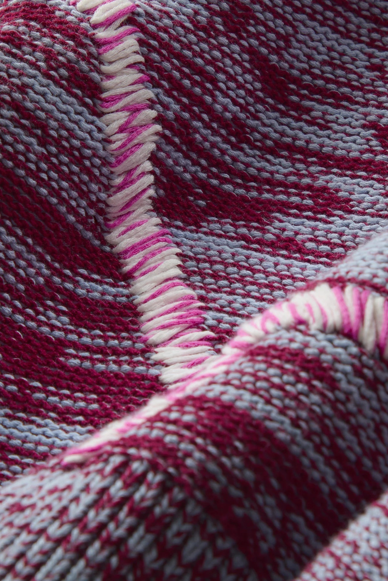 Close-up of a woven textile with a striped pattern in deep magenta, light gray, and white, showing the texture and a fringed edge.