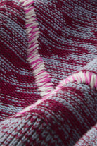 Close-up of a woven textile with a striped pattern in deep magenta, light gray, and white, showing the texture and a fringed edge.
