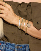 Close-up of a person's wrist wearing multiple gold bracelets with different designs, against a brown jacket background.