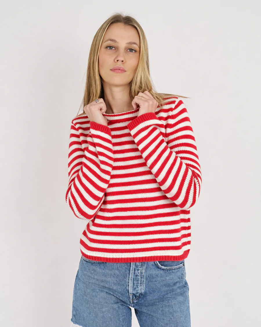 Person wearing a red and white striped sweater with blue jeans on a plain background