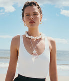 Woman wearing a white tank top and necklace on a beach