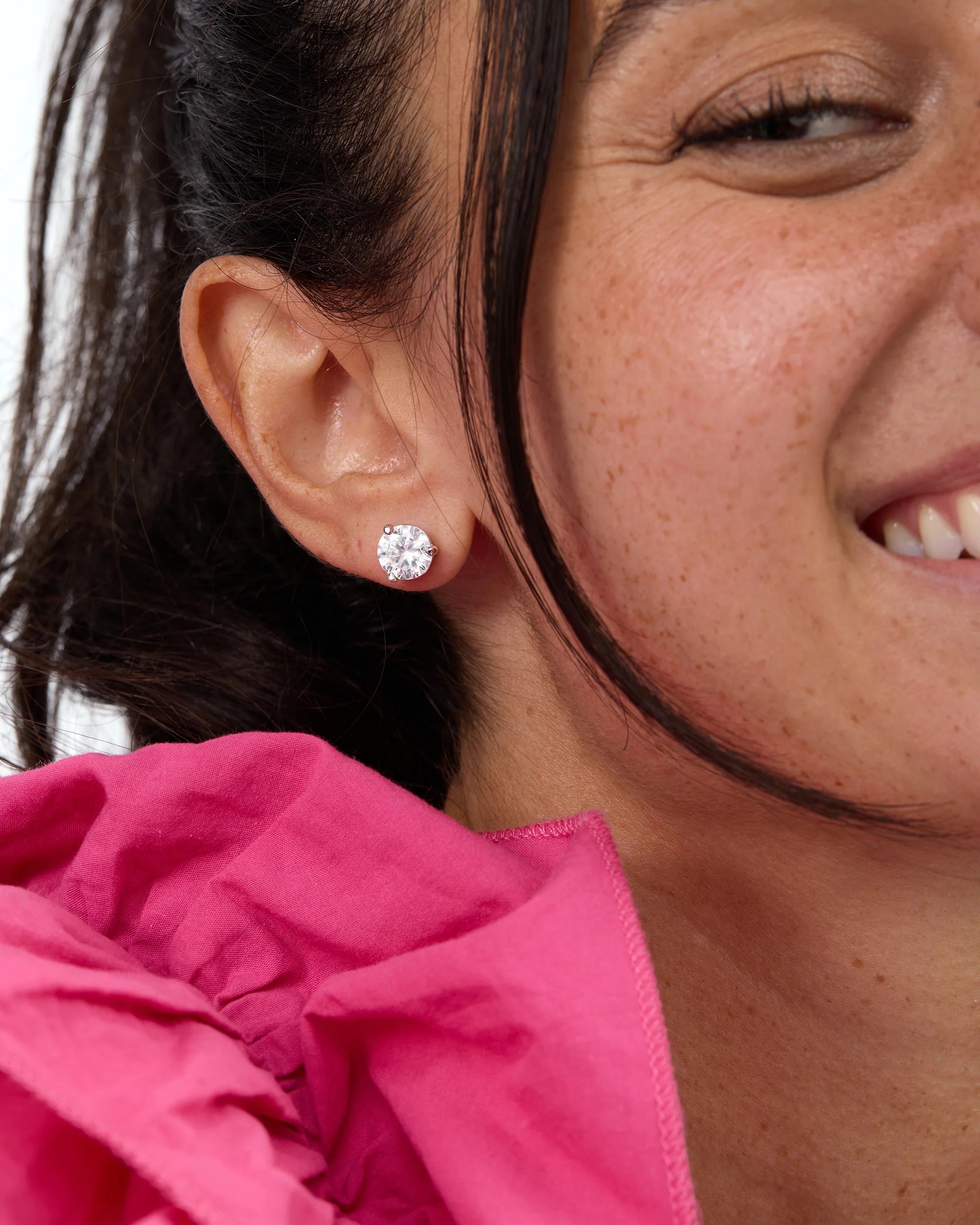 Close-up of a woman wearing diamond stud earrings with a pink garment.