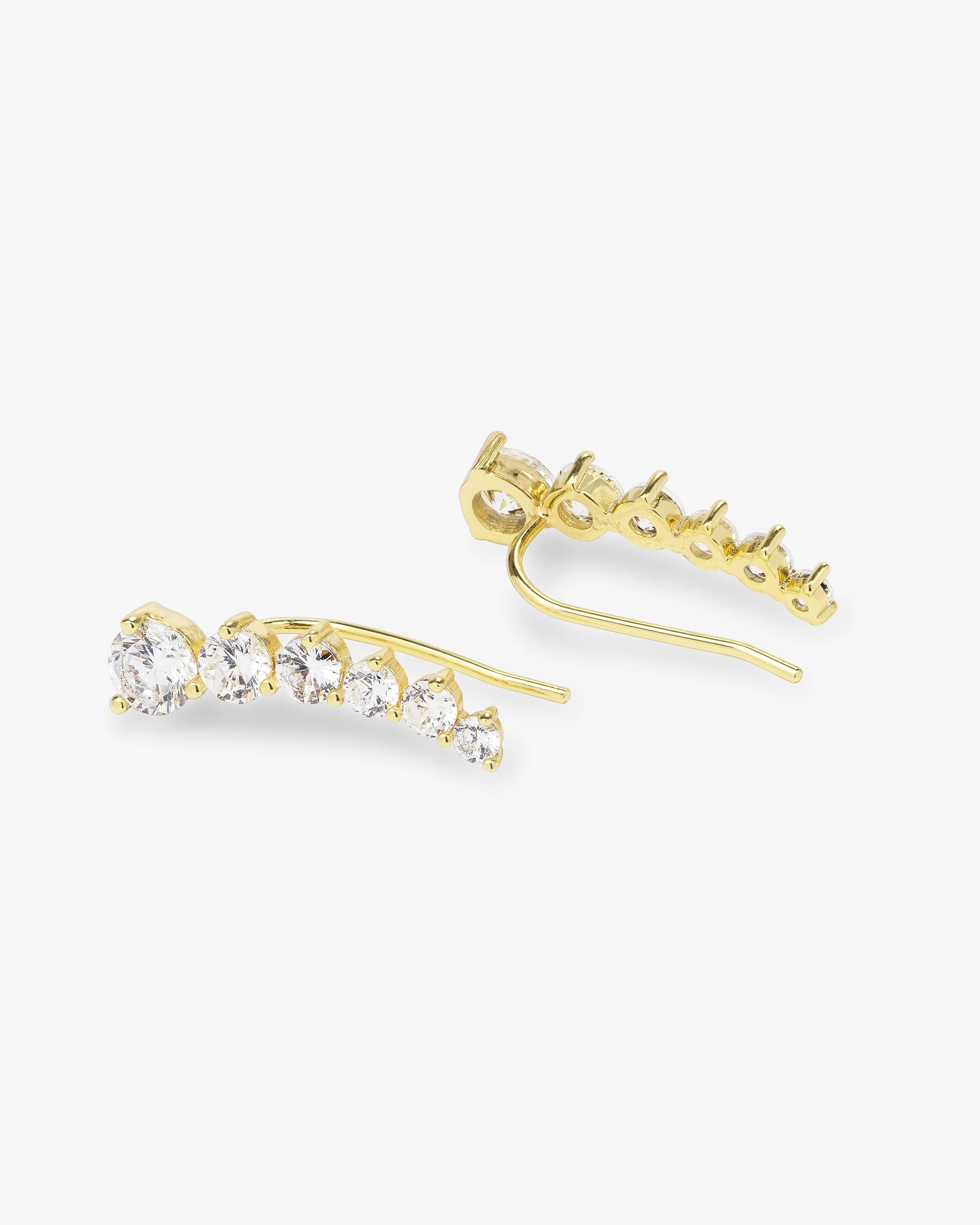 A pair of gold ear cuffs with a row of clear round-cut gemstones, shown on a light gray background. One cuff is oriented horizontally to display the front view of the stones, while the other is angled vertically to show the back post and setting.