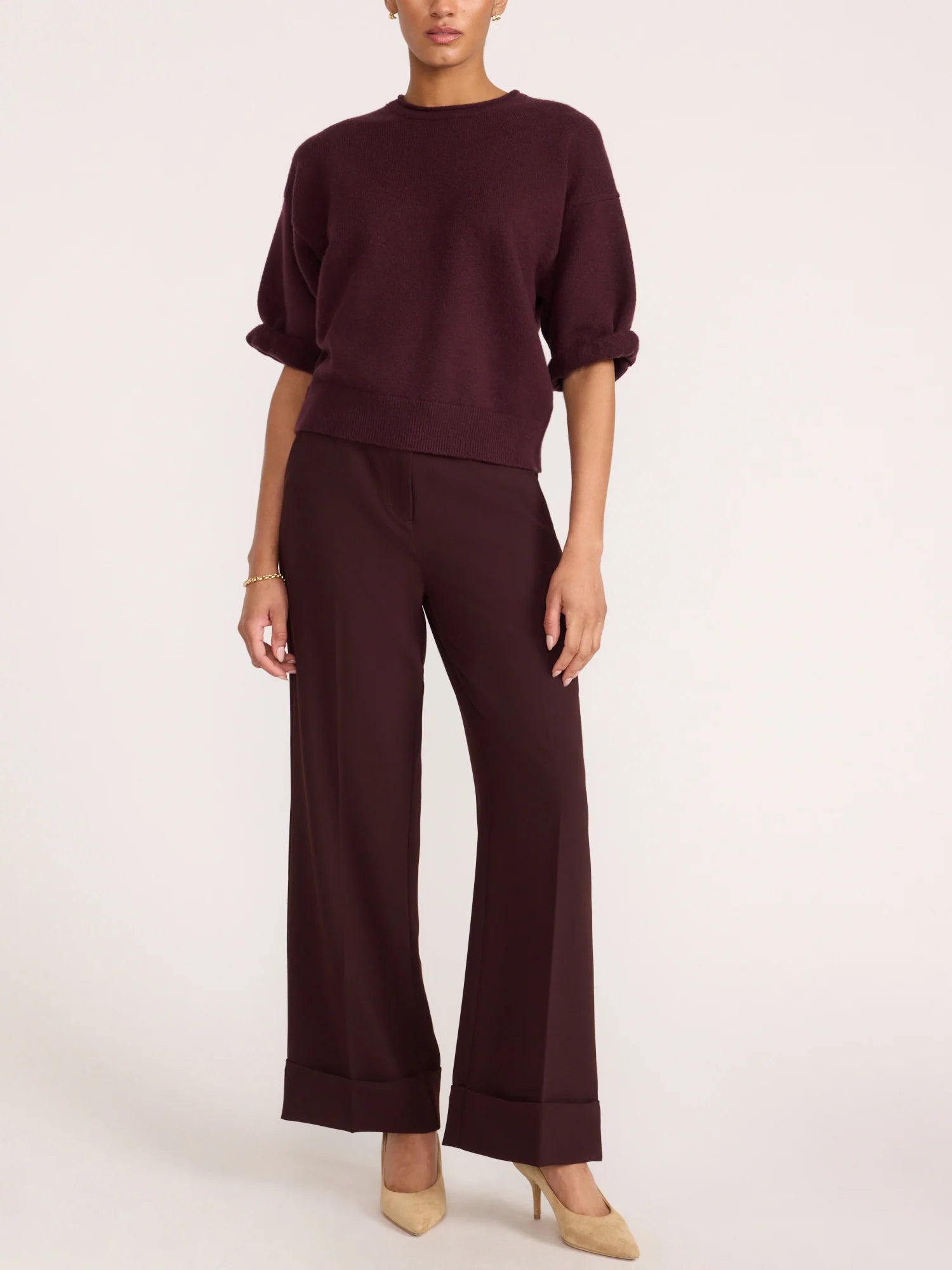 A model wearing a dark burgundy knit top with short puff sleeves and matching wide-leg trousers, paired with beige heels, against a plain light background.