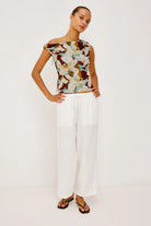 Woman wearing a floral top and white pants on a plain background