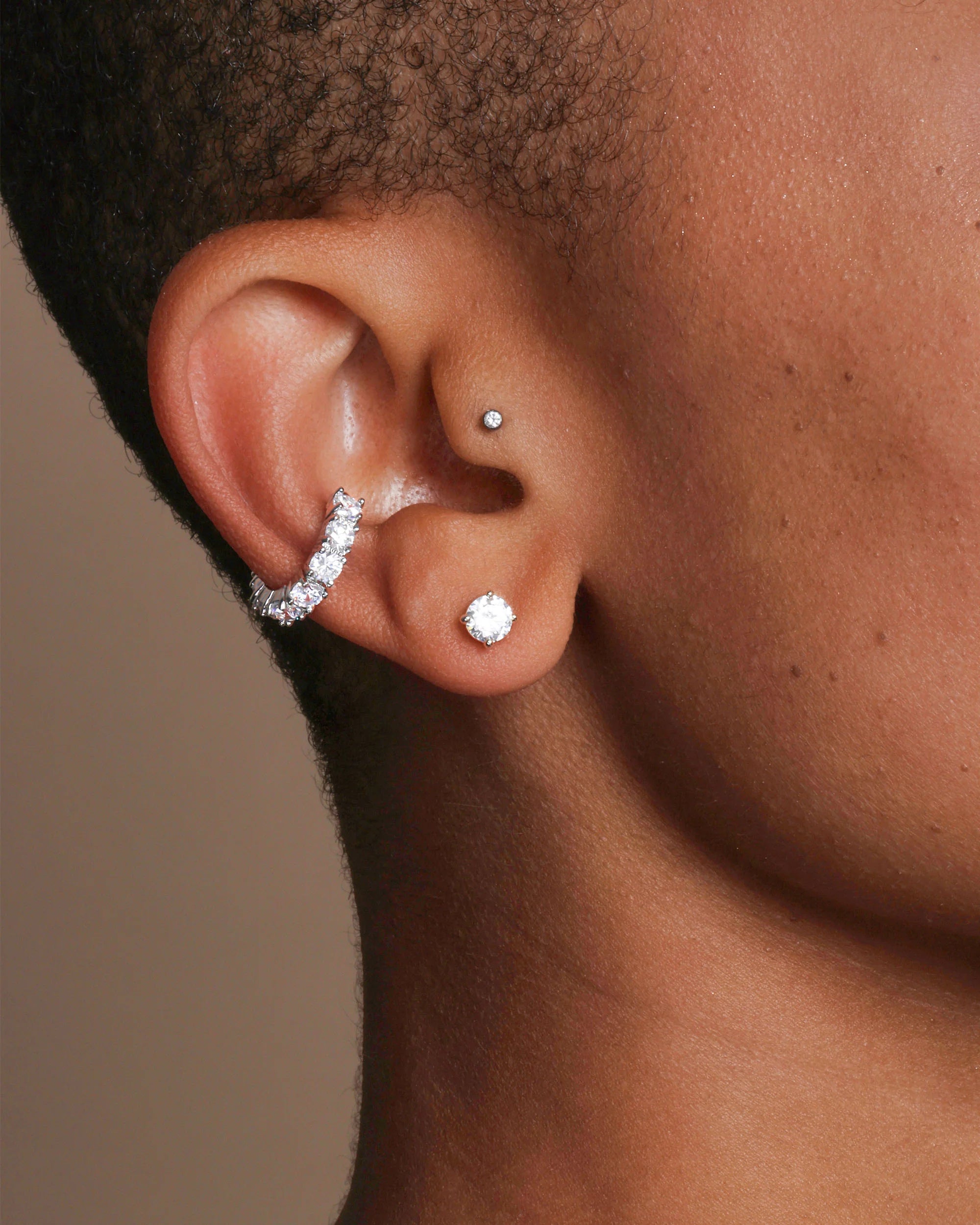 Close-up of an ear with diamond earrings on a neutral background
