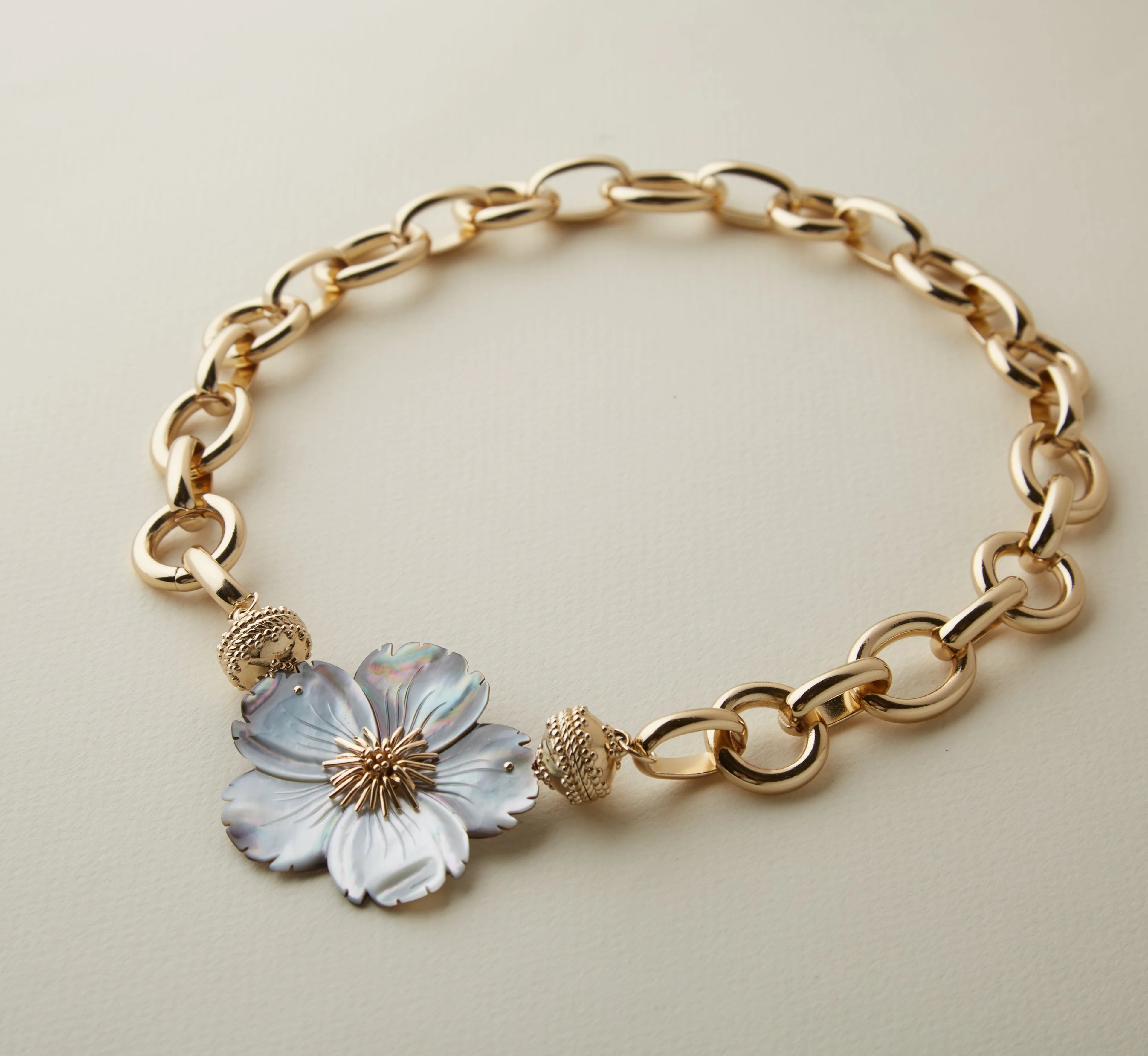 Gold chain bracelet with a floral charm on a light beige background