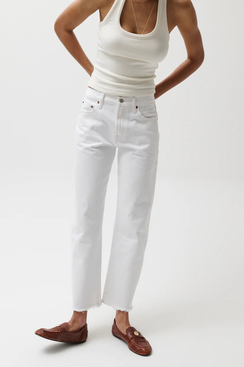 Person wearing a white tank top and white jeans on a plain background
