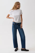 A woman modeling a white short-sleeve t-shirt and dark blue wide-leg jeans with black loafers, standing against a plain white studio background.