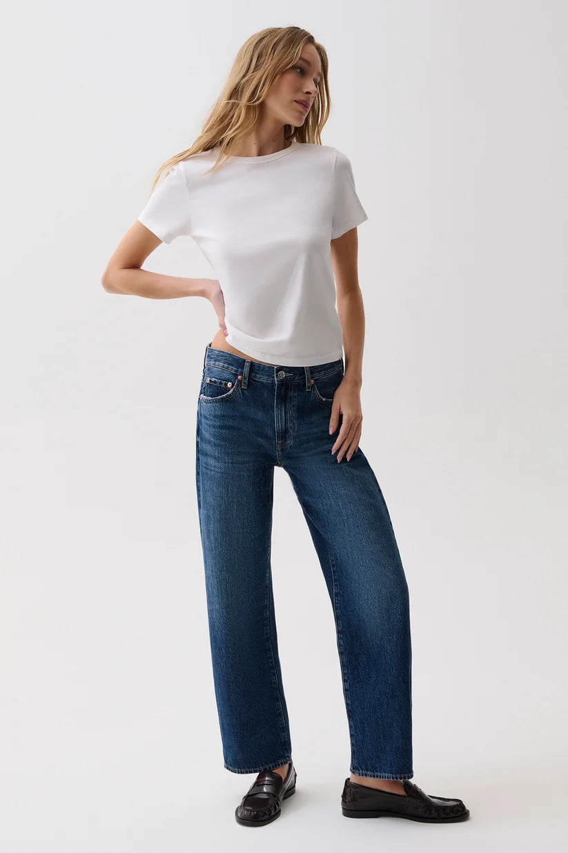 A woman modeling a white short-sleeve t-shirt and dark blue wide-leg jeans with black loafers, standing against a plain white studio background.