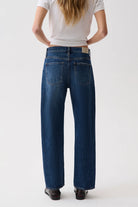 A model viewed from the back wearing a pair of dark blue wide-leg jeans, a white t-shirt, and dark brown shoes, set against a plain white studio background.