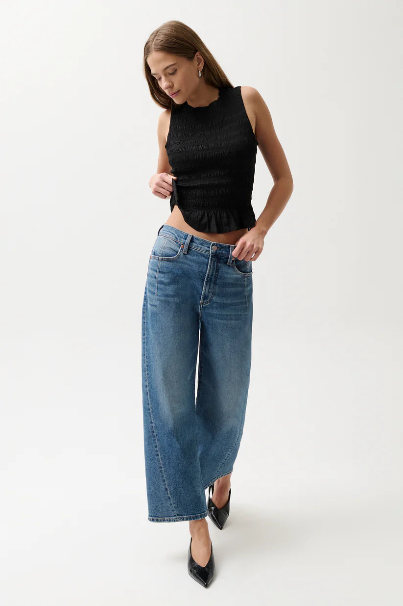 Woman wearing a black sleeveless top and blue jeans on a white background