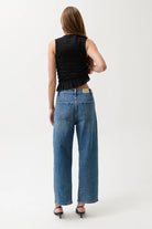 Person wearing blue jeans and a black sleeveless top on a white background