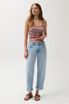 Woman wearing a striped tank top and light blue jeans on a white background