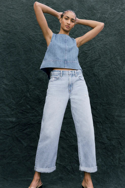 Woman wearing a denim top and light blue jeans against a dark textured background