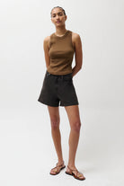 Person wearing a brown sleeveless top and black shorts on a white background