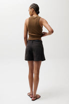 Person wearing a brown sleeveless top and black shorts on a white background