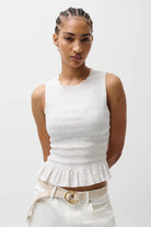 Woman wearing a white sleeveless top with a peplum waist and white pants on a white background