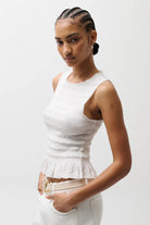 Woman wearing a white sleeveless top against a plain background