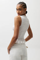 Woman wearing a white sleeveless top and pants on a plain background