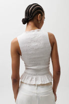 Person wearing a white sleeveless top with ruffled details on a plain background