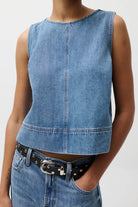 Woman wearing a denim sleeveless top and jeans on a plain background