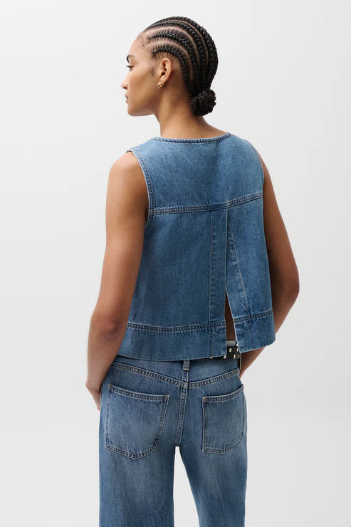 Person wearing a denim vest and jeans on a plain background