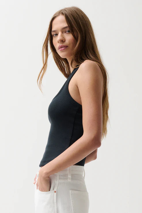 Woman wearing a black sleeveless top and white pants against a plain background