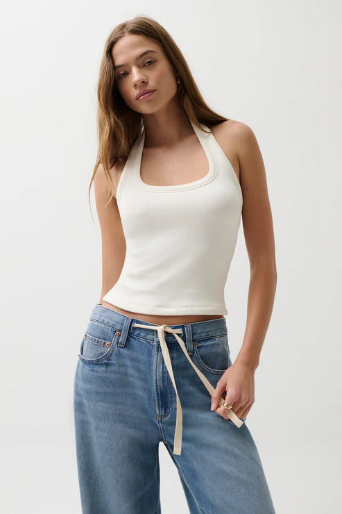 Woman wearing a white tank top and blue jeans against a plain background