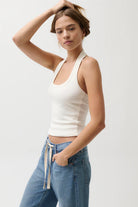 Woman wearing a white halter top and blue jeans on a plain background